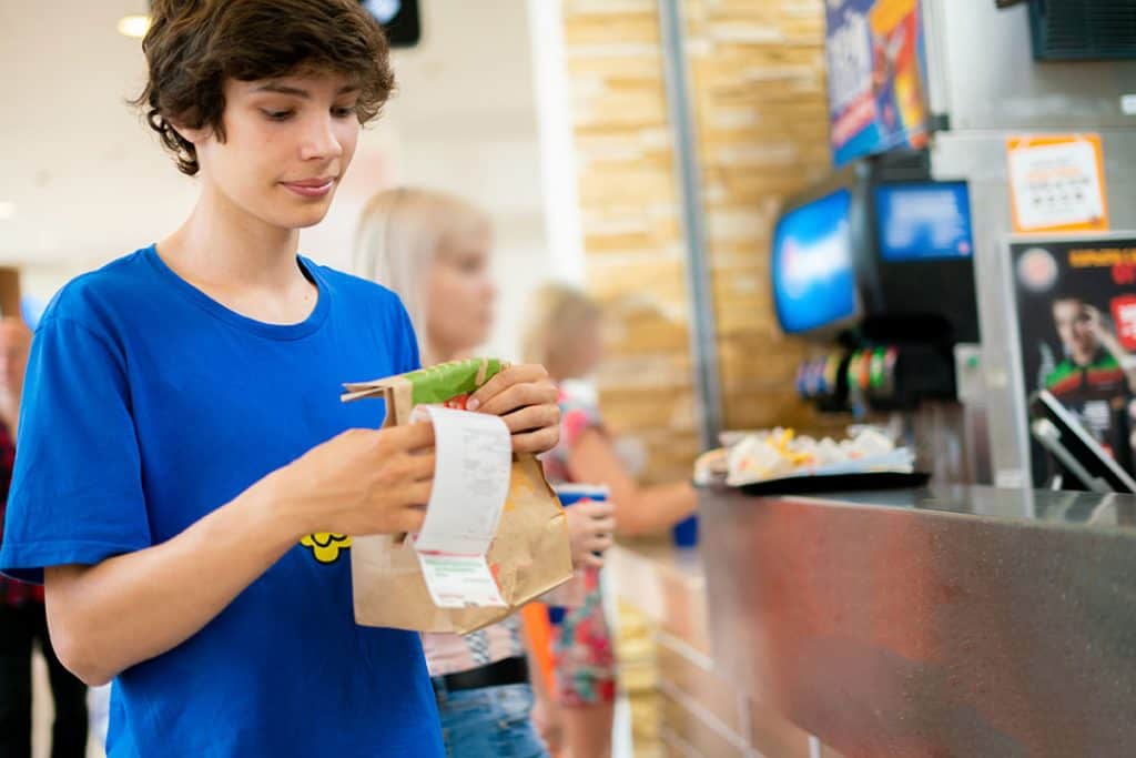 young man received his to go food order in fast food restaurant and looks at receipt