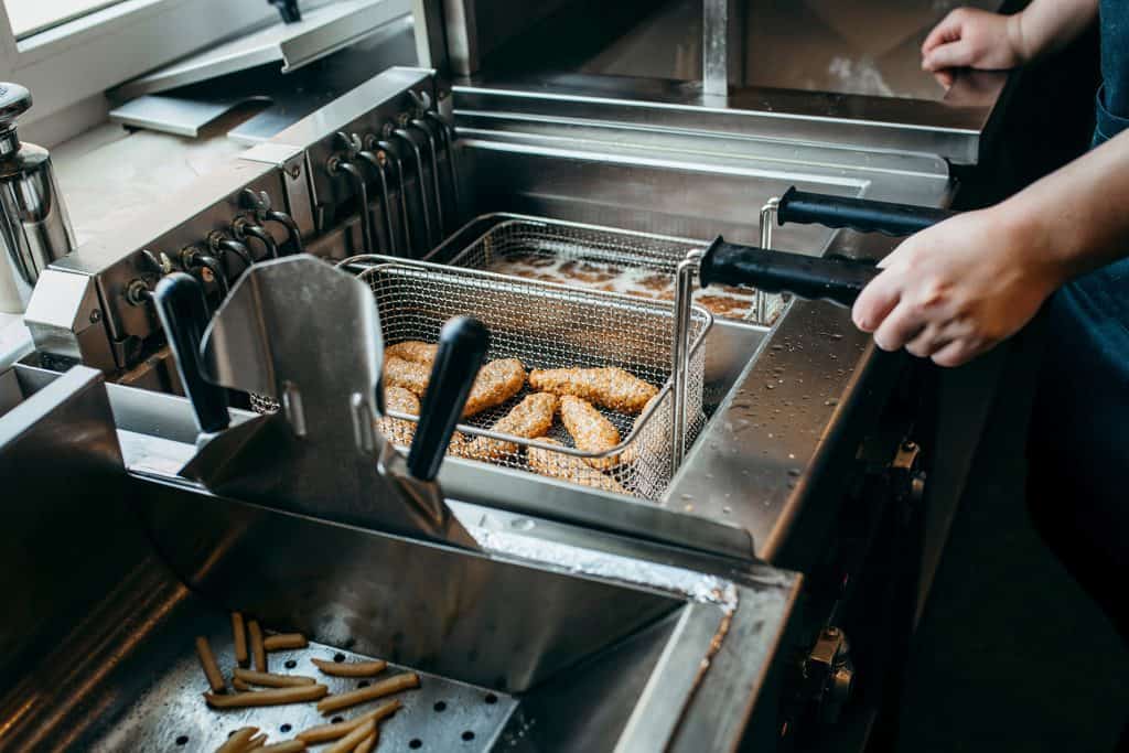 Fryer cook pulls timed chicken wings in a basket from fryer oil