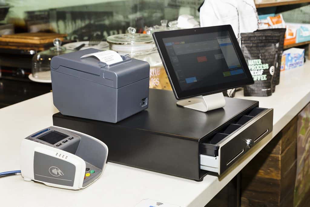 POS terminal consisting of Tablet computer with touchscreen, mobile printer and pay terminal on a cashbox at a counter in regular retail coffee shop.