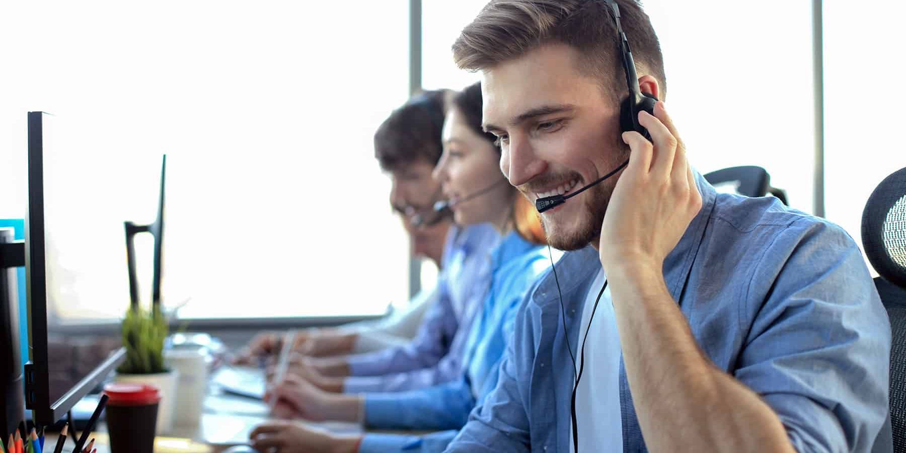 Portrait of call center worker accompanied by his team. Smiling customer support operator at work